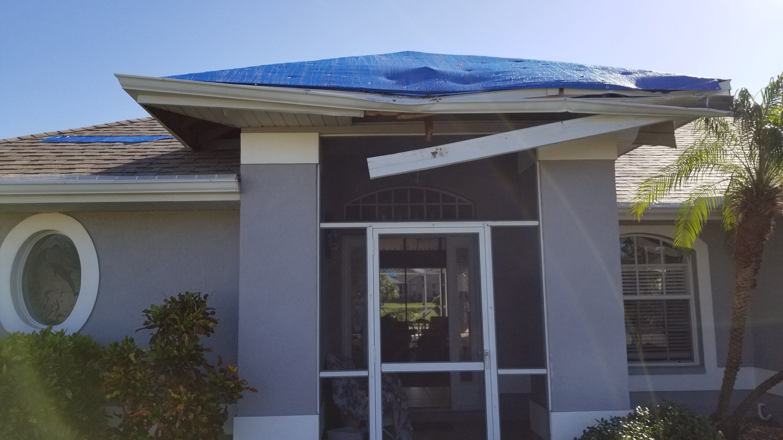 Front of home with temporary tarp covering roof after tree impact.