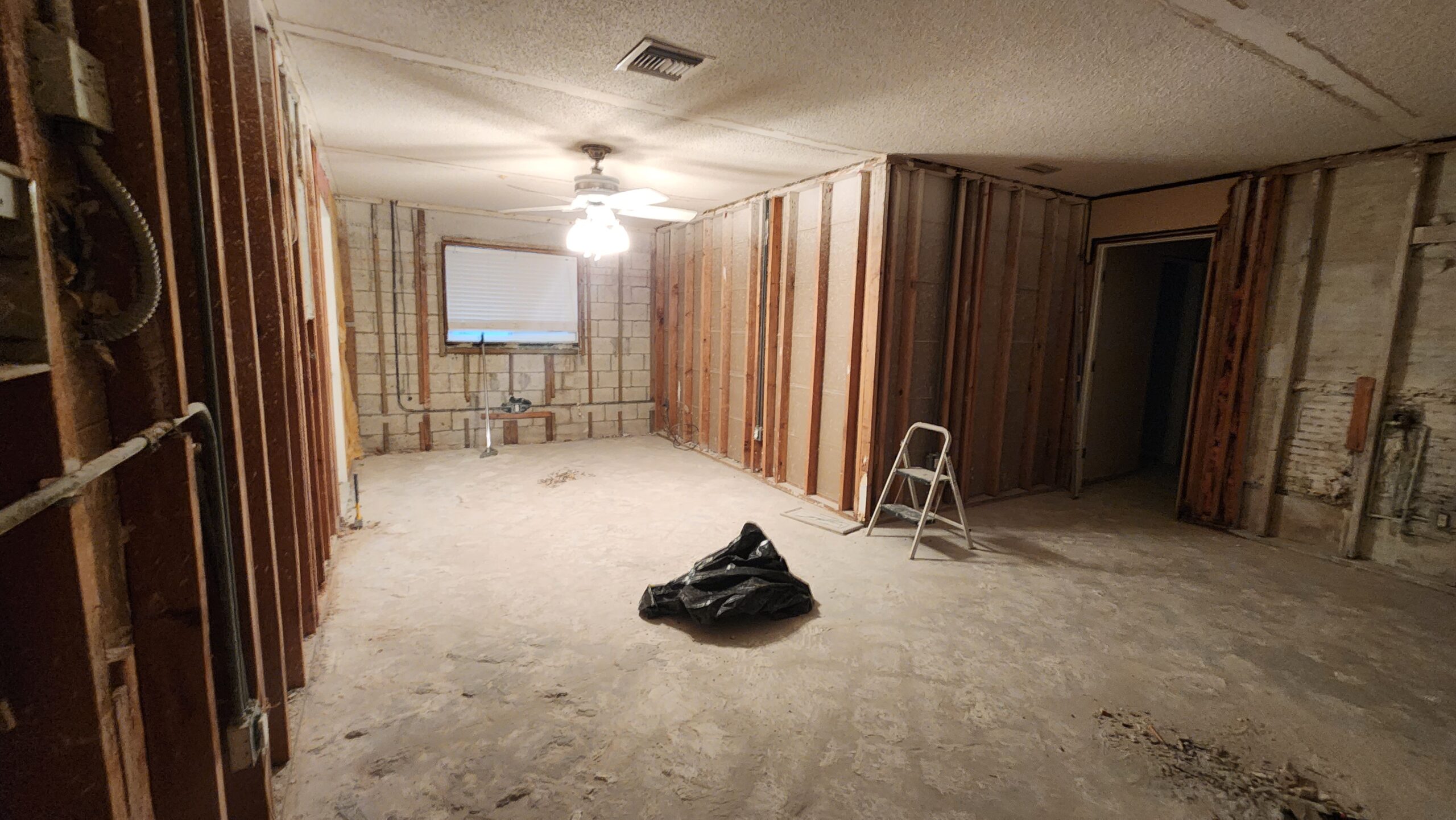Interior renovation in progress showing exposed framing, uneven floor, and wall damage prior to remodel.
